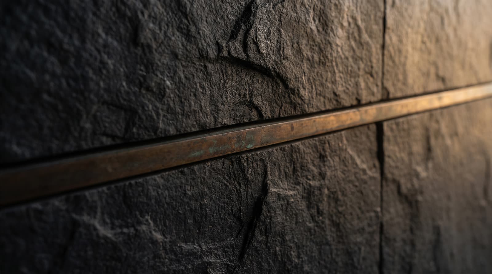 Warm light on raw honed stone with a thin bronze seam