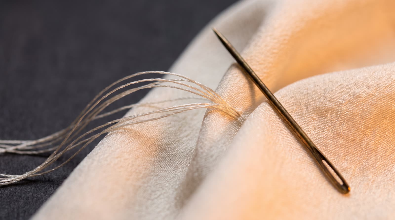 Ivory silk thread being stitched with a bronze needle